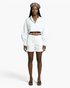 Beach Rose Co. white cropped blouse with balloon sleeves, smocked cuffs, and button front worn with white shorts.