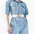 Beach Rose Co. white elastic waist belt with a gold geometric alloy buckle worn over a light blue denim jumpsuit.