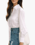 Beach Rose Co. white blouse with floral embroidery, pointed collar, and openwork sleeve details worn with blue jeans.