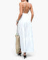 Beach Rose Co. white sleeveless maxi dress with an open back and tiered skirt, worn with a woven tote bag.