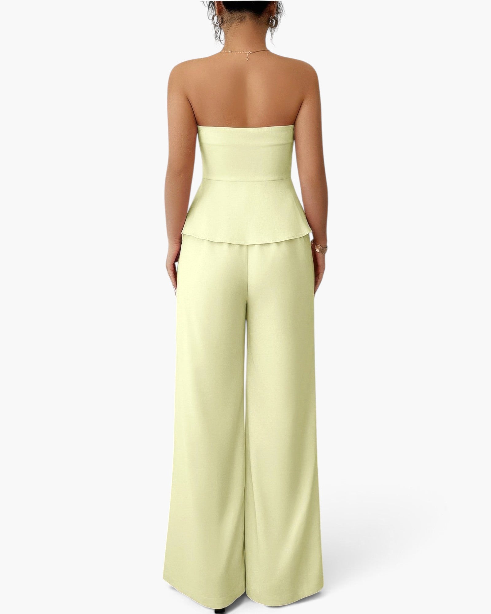 A woman shown from the back wearing a strapless pale yellow-green set with a structured waistband and wide legs, photographed against a clean white studio background.