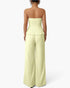 A woman shown from the back wearing a strapless pale yellow-green set with a structured waistband and wide legs, photographed against a clean white studio background.