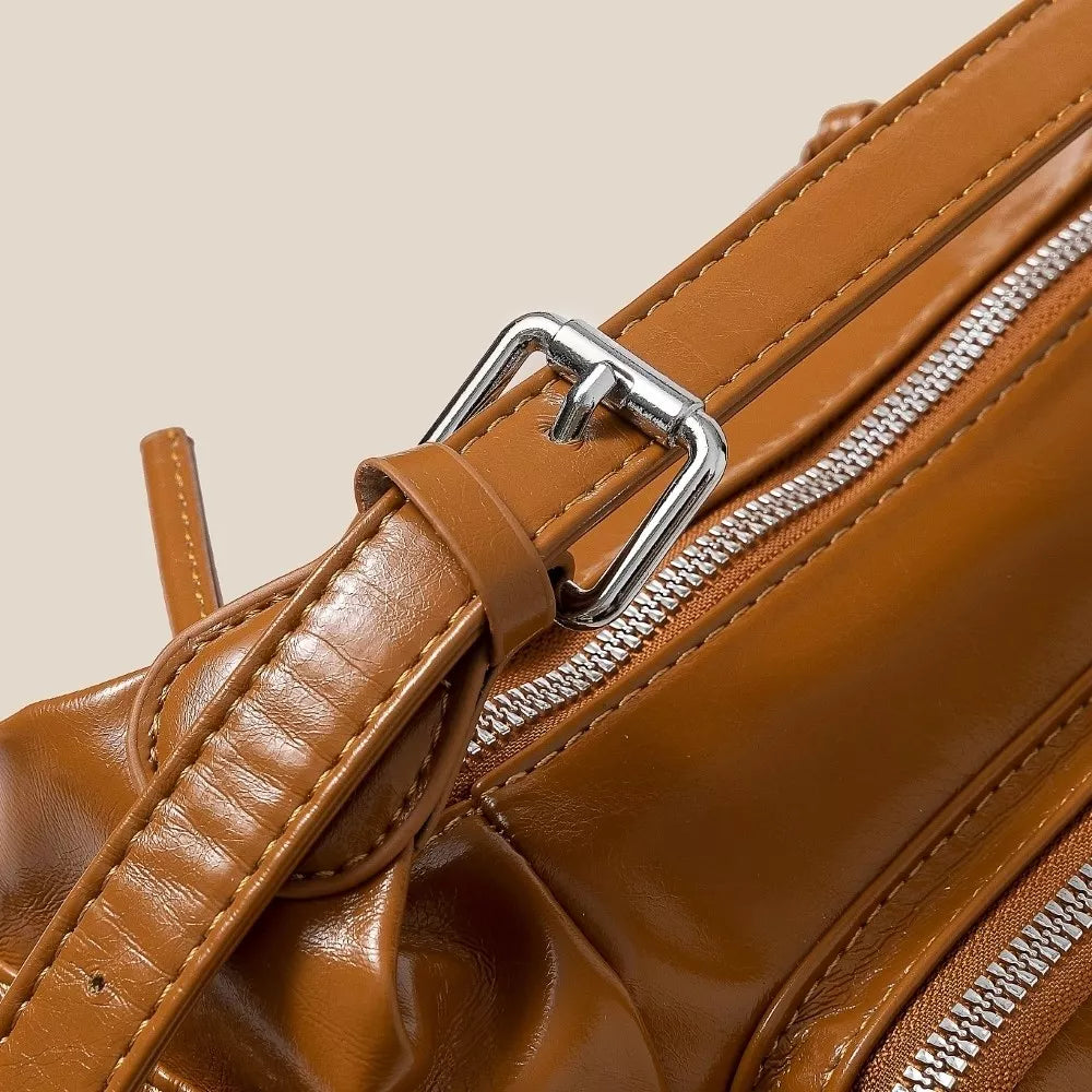 Close-up of a brown leather bag with a silver buckle and zipper.