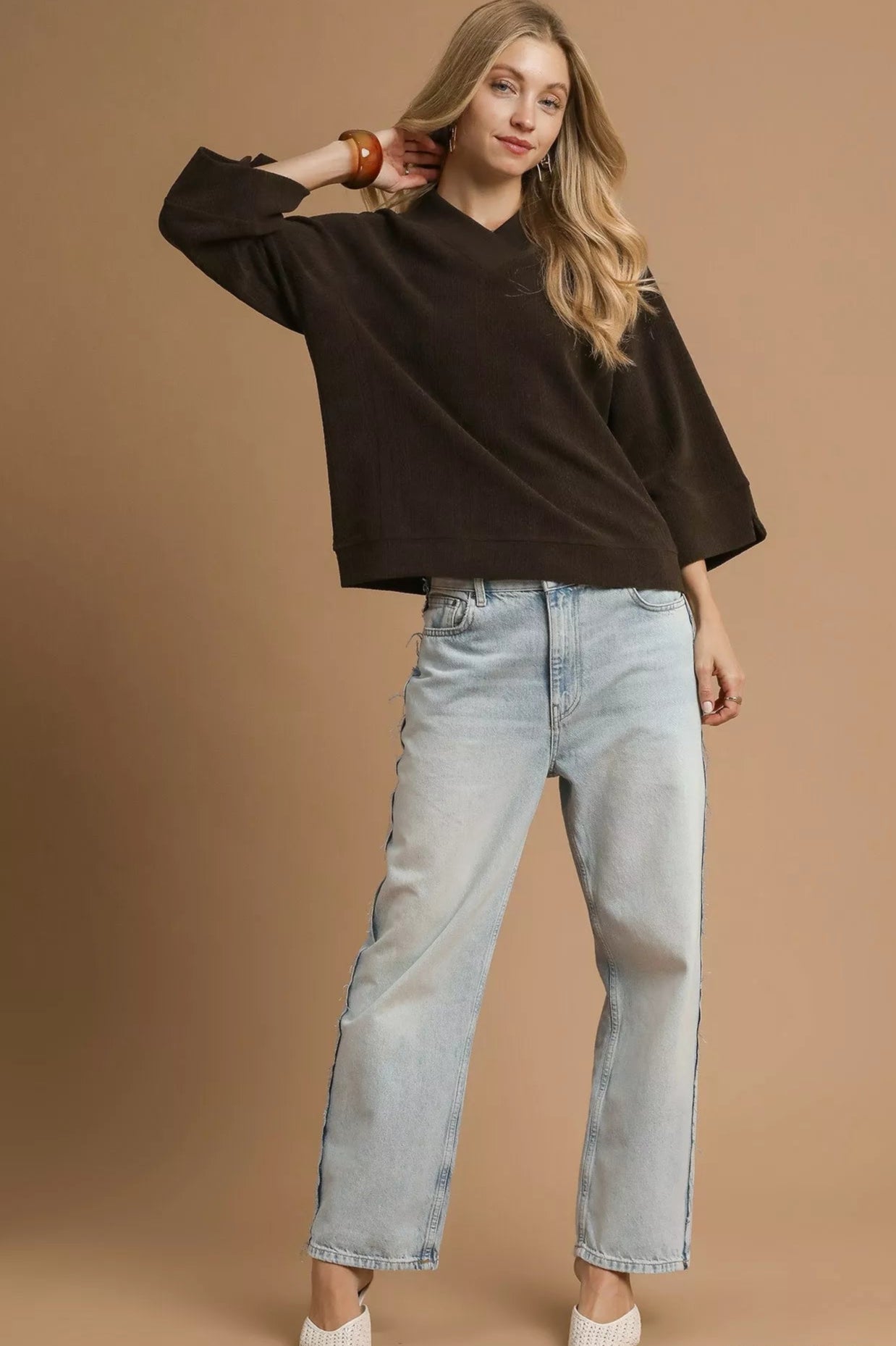 Woman wearing a black sweater and light blue jeans against a brown background