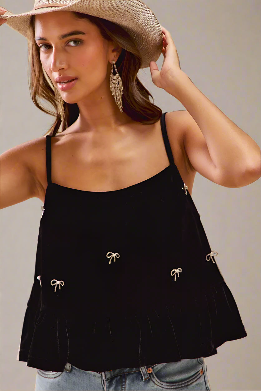 Woman wearing a black top with bow details and a straw hat on a beige background