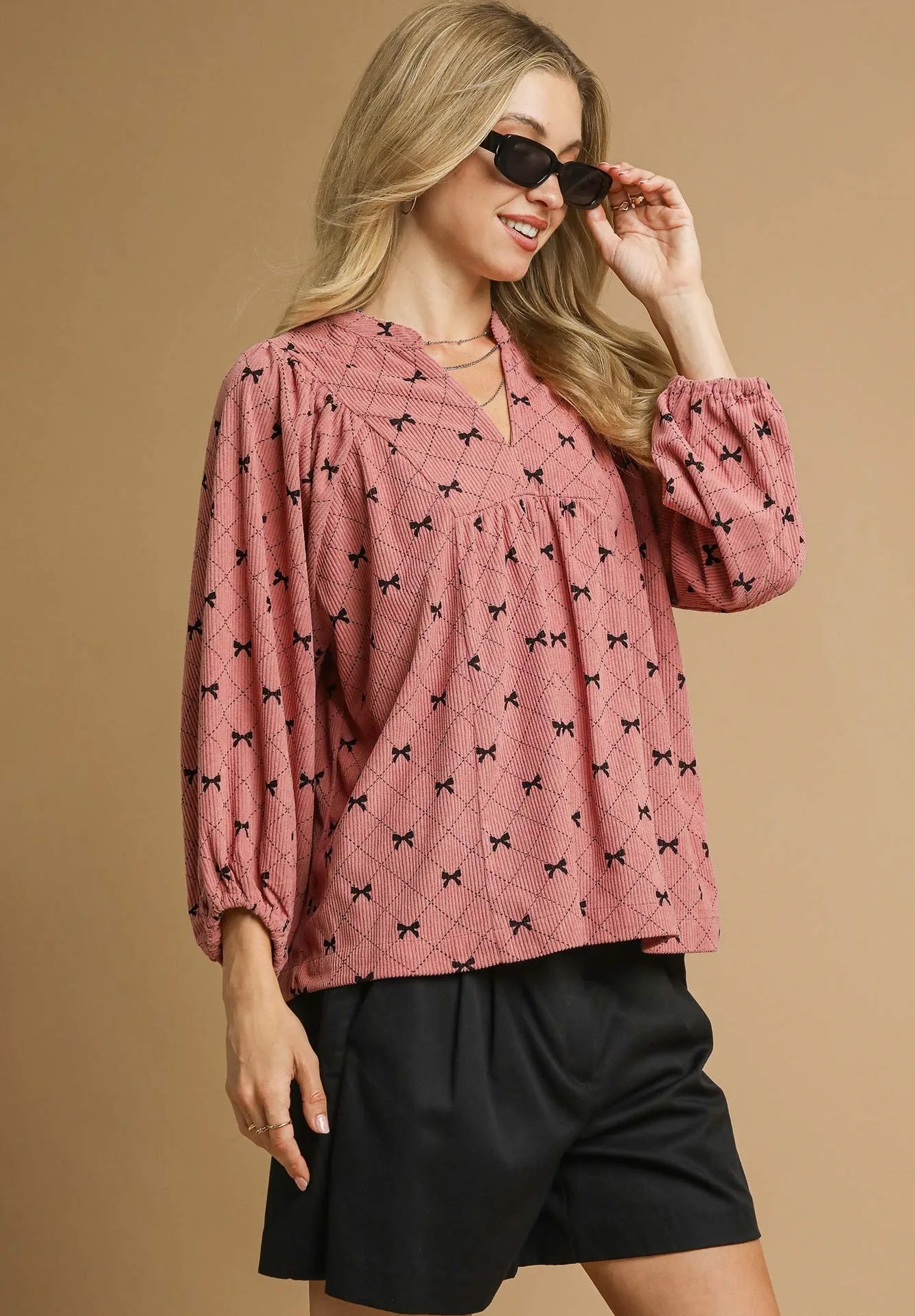 Woman wearing a pink blouse with black patterns and black shorts on a beige background