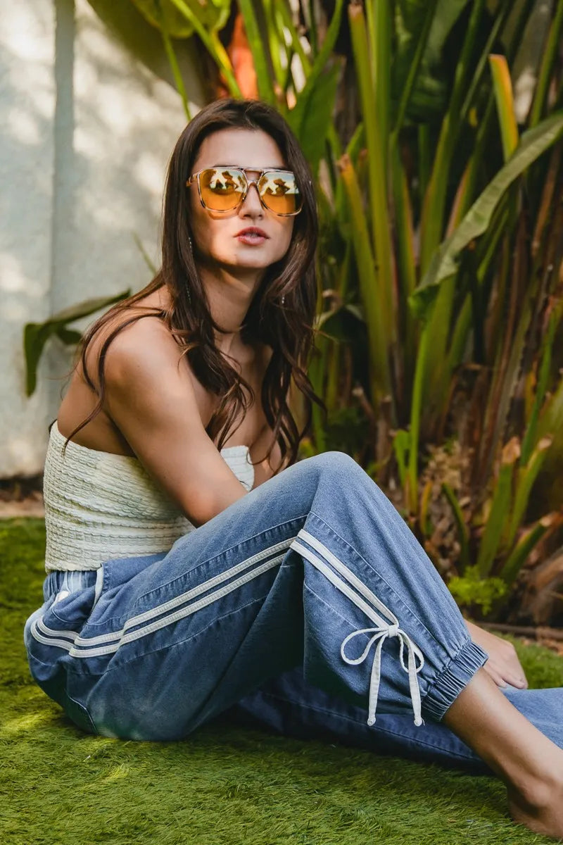 Woman sitting outdoors wearing sunglasses and a casual outfit with plants in the background