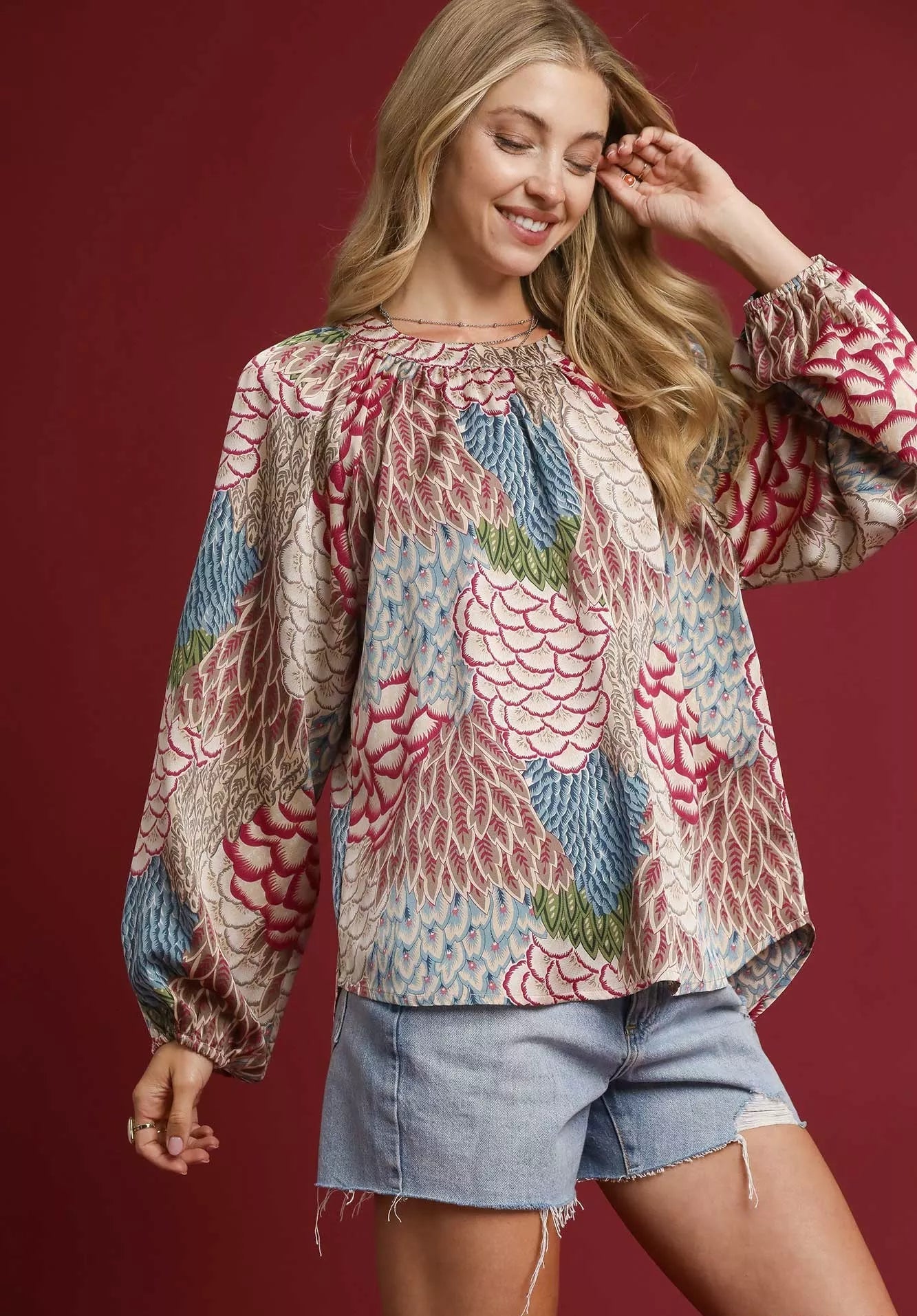 Woman wearing a colorful patterned blouse with denim shorts on a red background