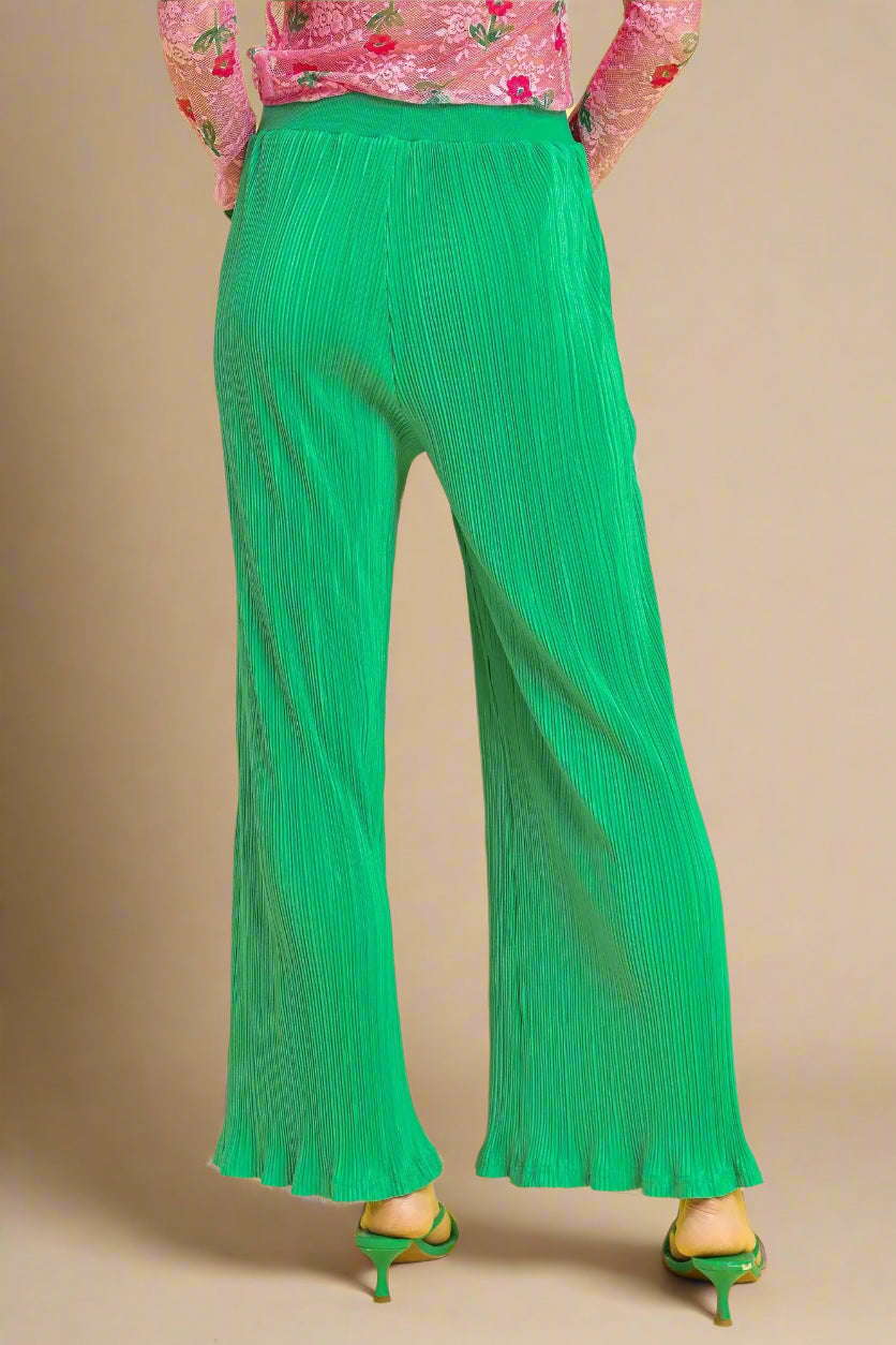 Green pleated pants worn by a person on a beige background