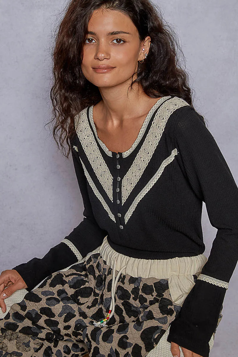 Woman wearing a black cardigan with white trim and leopard print pants against a gray background