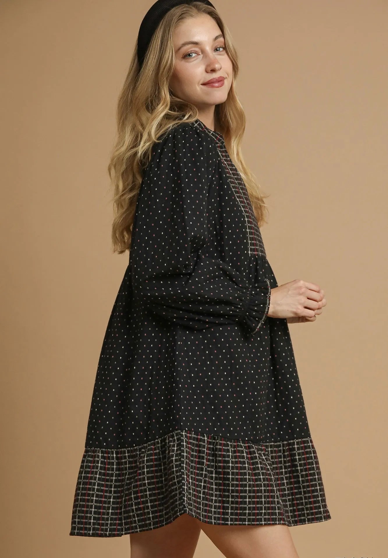 Woman wearing a black dress with white polka dots and plaid hem on a beige background