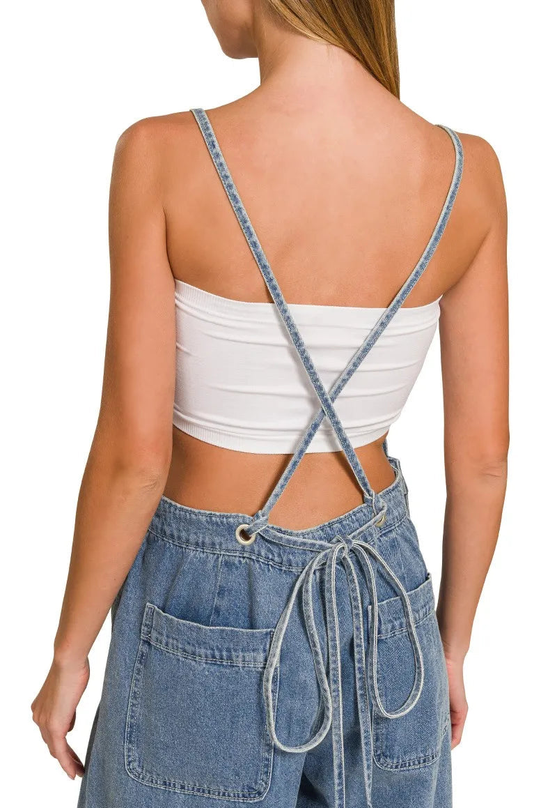 Person wearing a white crop top and blue denim overalls on a white background