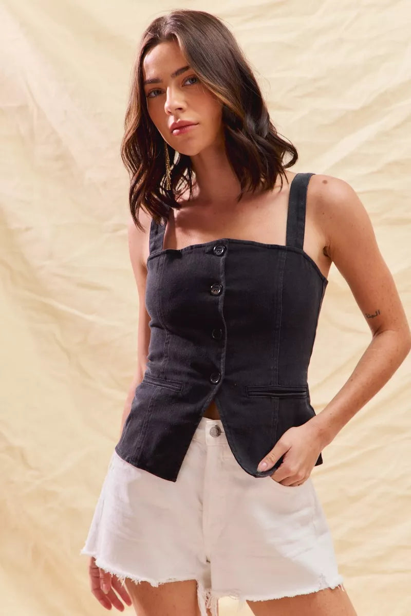 Woman wearing a black denim corset top and white shorts against a beige background