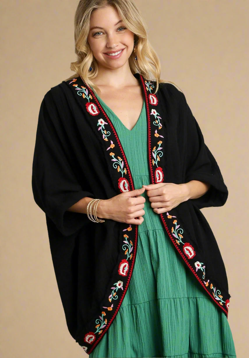 Woman wearing a black embroidered cardigan over a green dress on a plain background