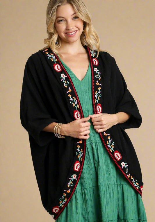 Woman wearing a black embroidered cardigan over a green dress on a plain background