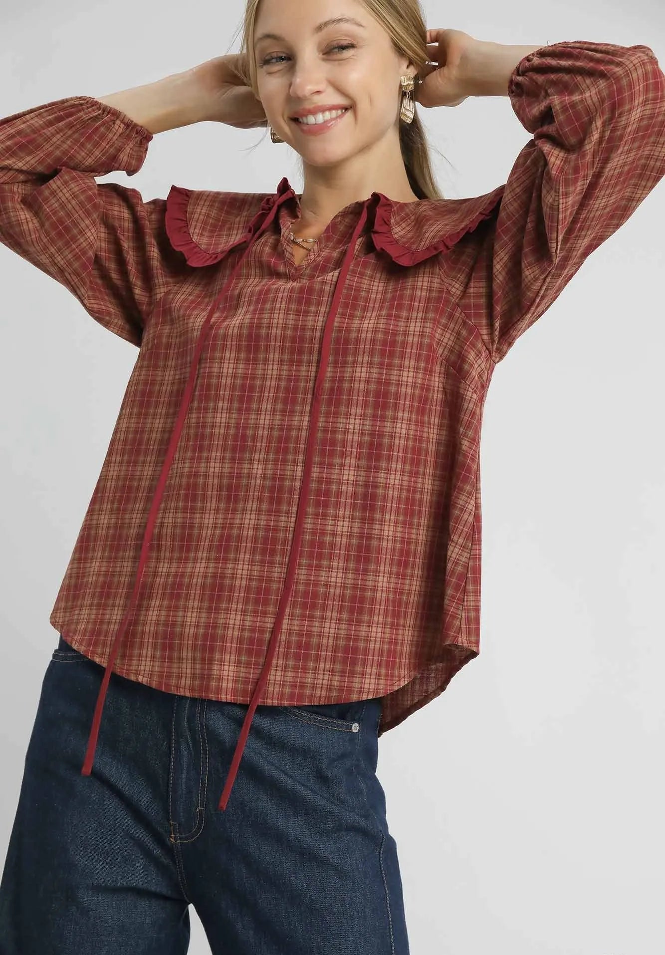 Woman wearing a red plaid shirt with ruffled collar on a gray background