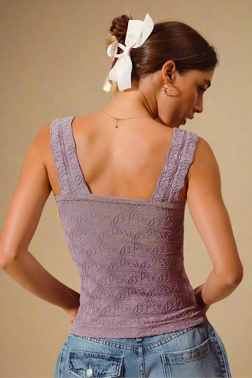 Woman wearing a textured purple top and blue jeans against a beige background