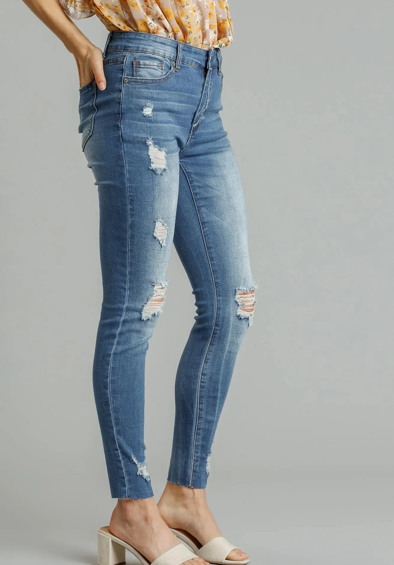 Blue distressed jeans worn by a person on a gray background