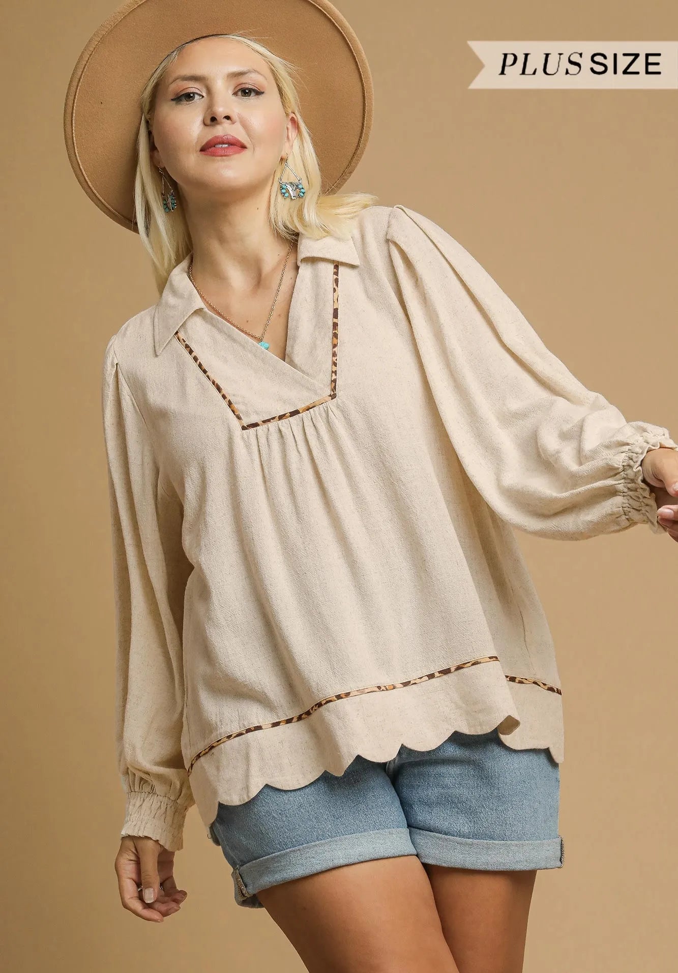Woman wearing a beige blouse with scalloped edges and denim shorts on a beige background.
