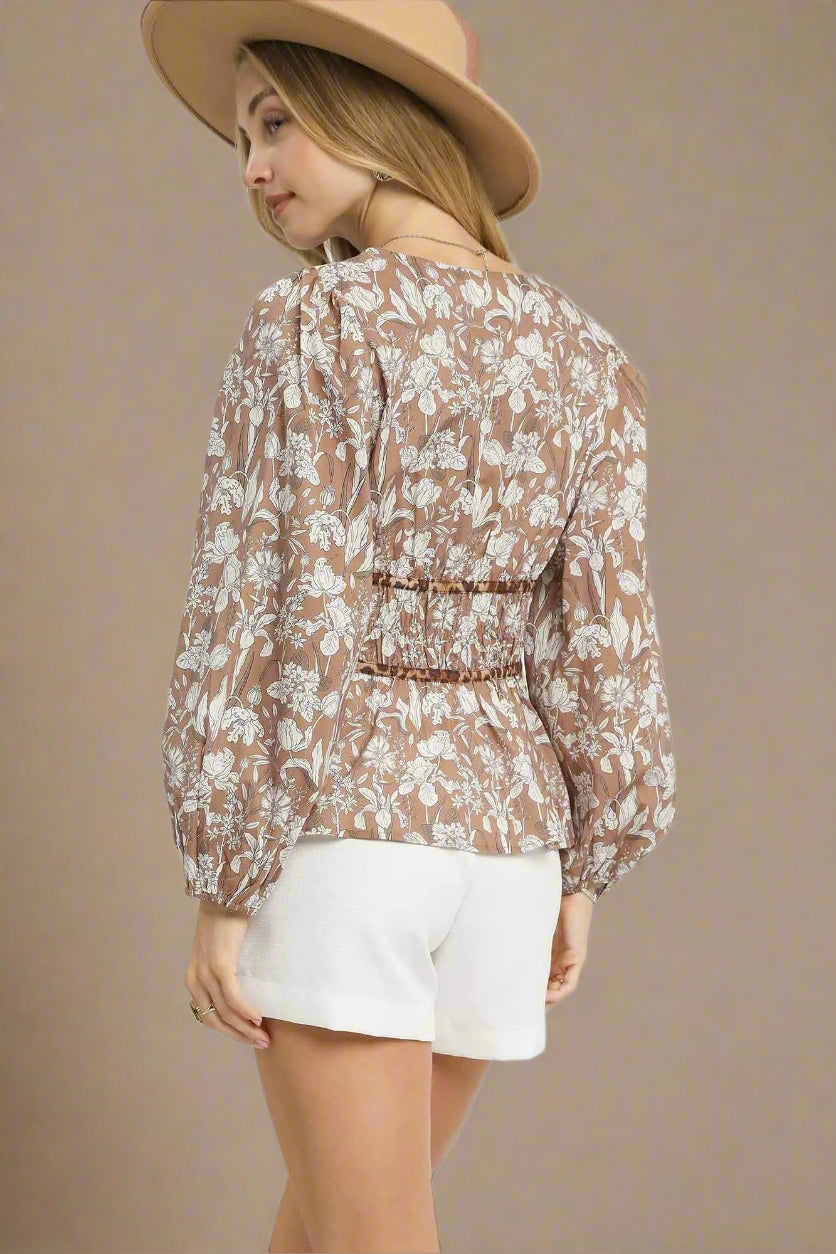 Woman wearing a light brown floral blouse and white shorts on a beige background
