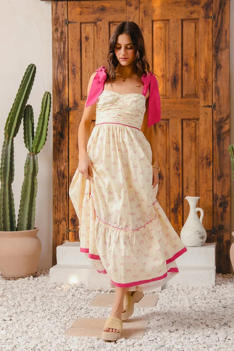 Woman in a cream dress with pink accents standing in front of a wooden door with a cactus plant in the background.