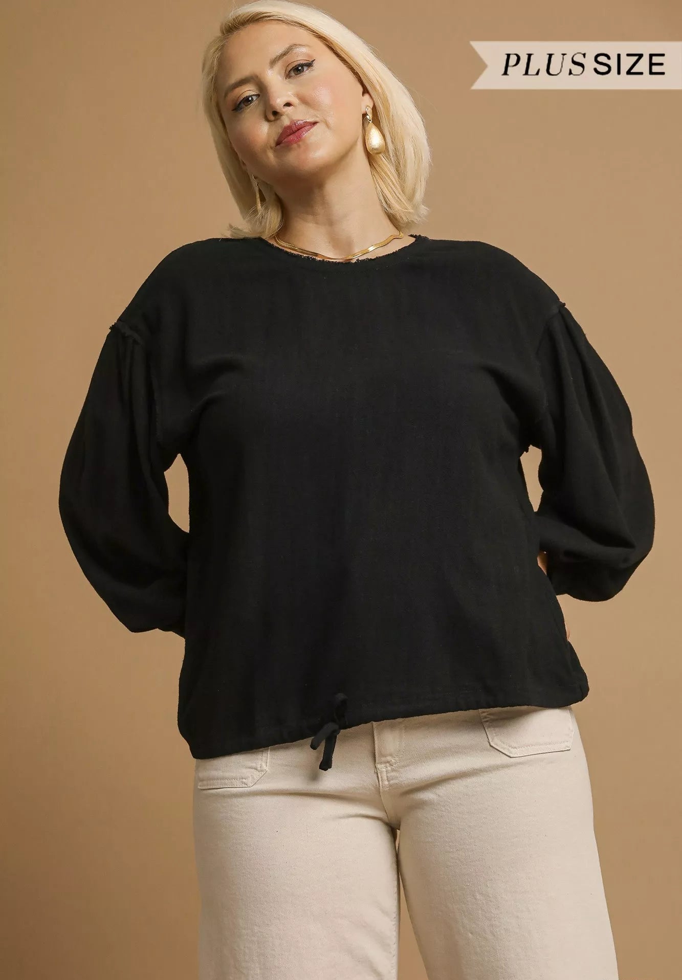 Woman wearing a black plus-size sweater and beige pants on a beige background