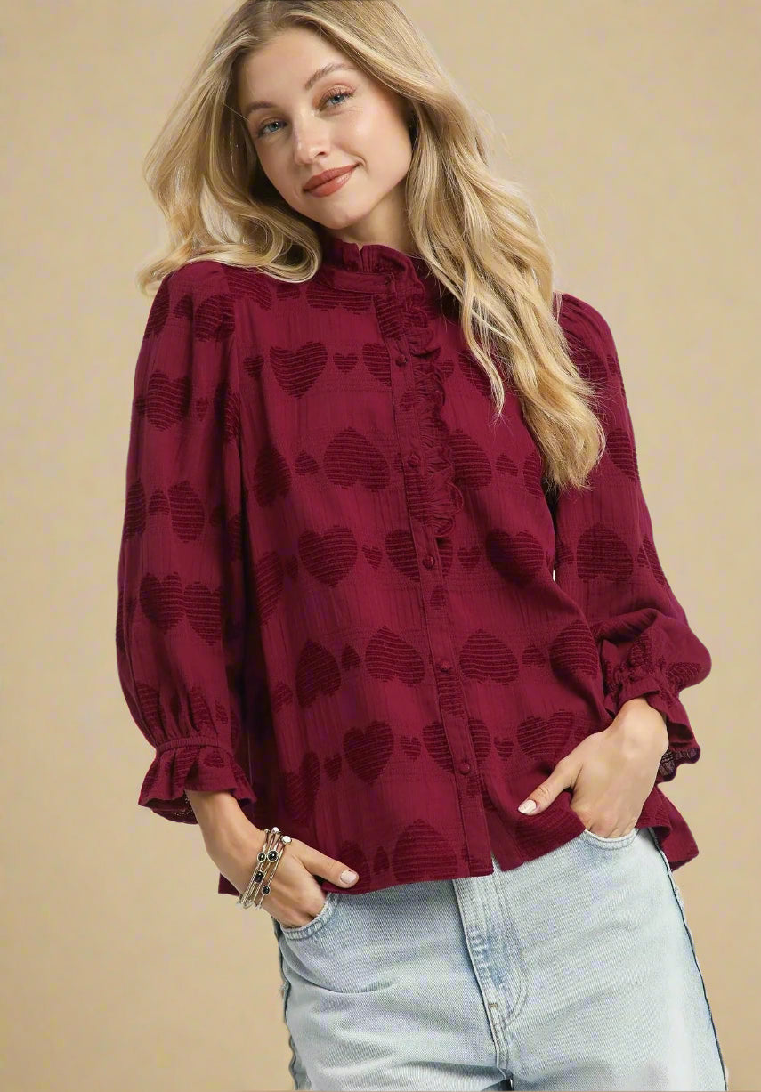 Woman wearing a burgundy blouse with heart patterns and light blue jeans on a white background