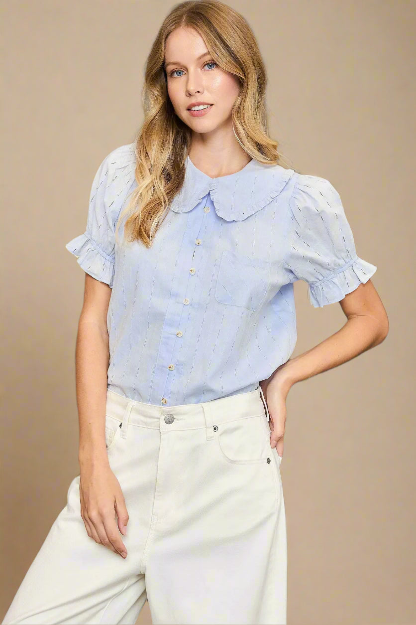 Woman wearing a light blue blouse with ruffled sleeves and collar against a beige background