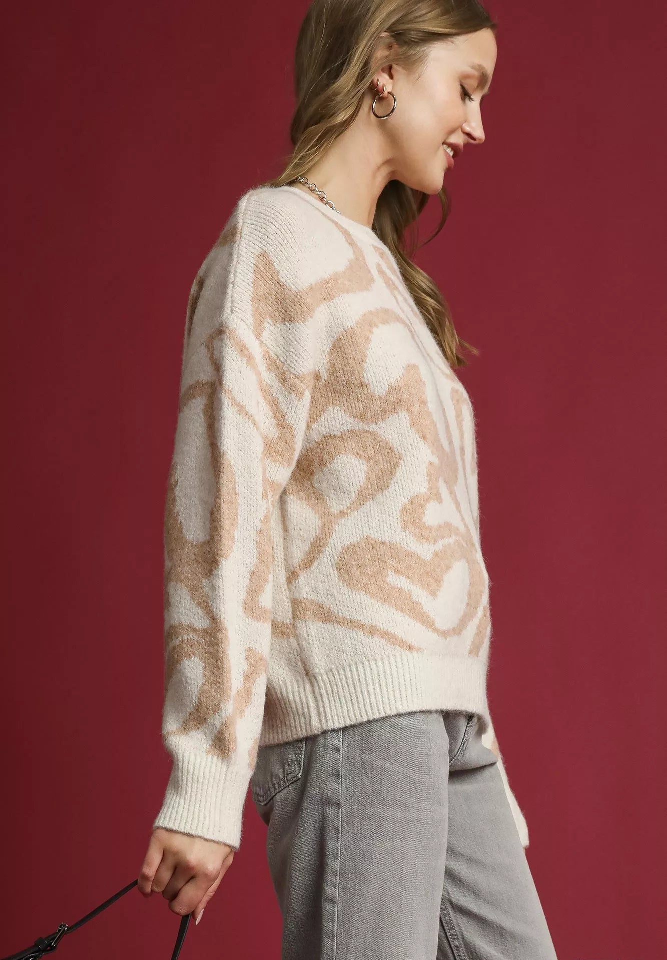 Woman wearing a cream sweater with a pattern against a red background