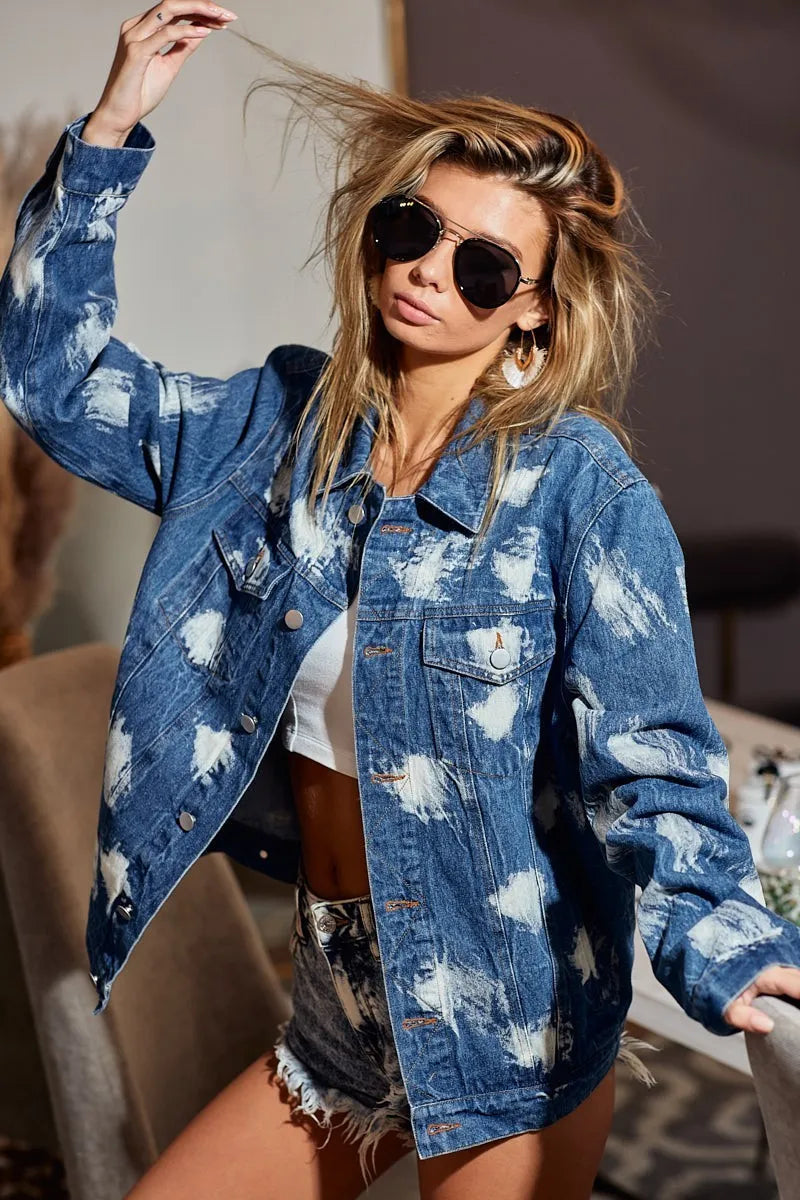 Woman wearing a blue denim jacket with white cloud patterns, sunglasses, and denim shorts indoors.