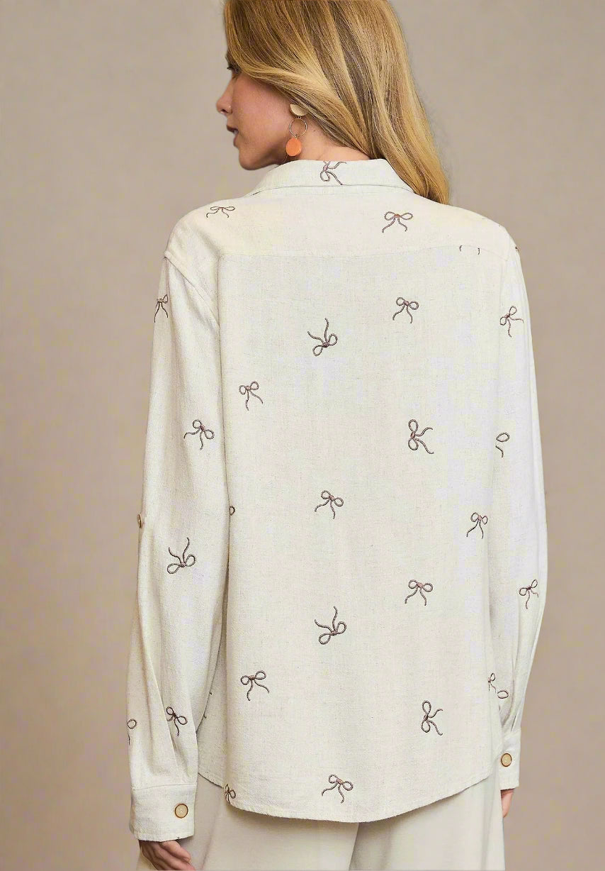 Woman wearing a cream-colored blouse with bow pattern on a gray background