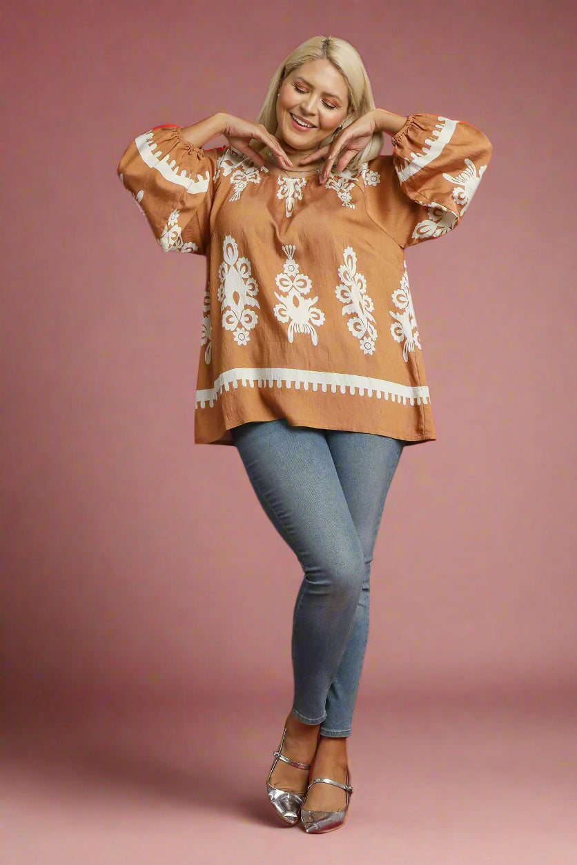 Woman wearing a brown blouse with white embroidery and blue jeans on a red background