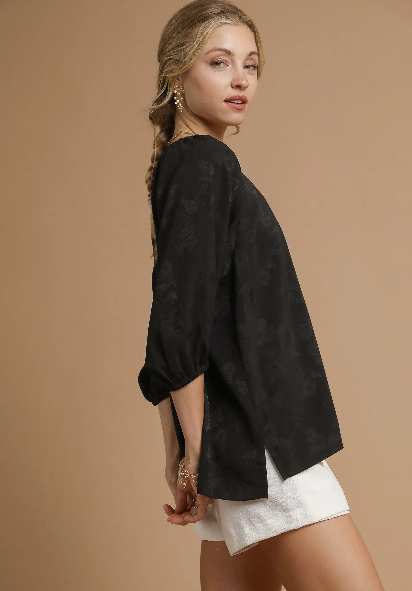 Woman wearing a black jacket and white shorts on a beige background