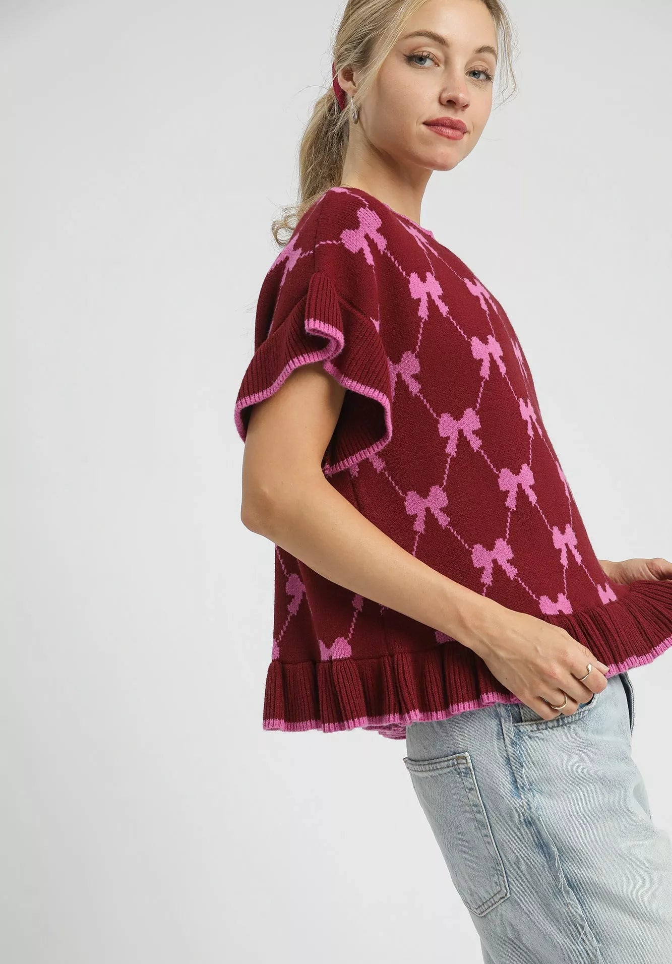 Woman wearing a burgundy sweater with pink bow patterns on a white background