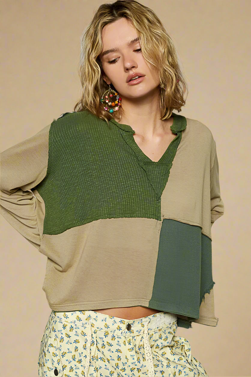 Woman wearing a green and beige sweater with floral pants against a plain background