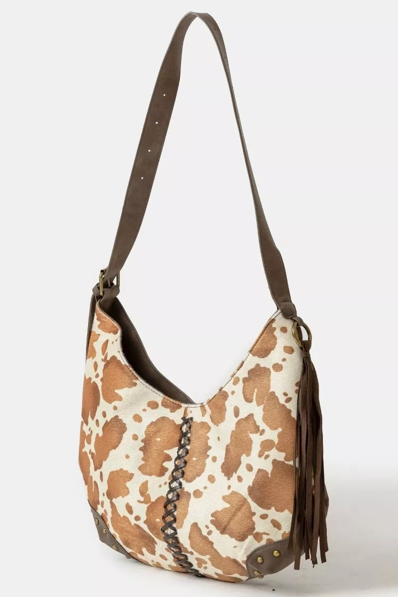 cow print handbag with brown leather strap on a white background