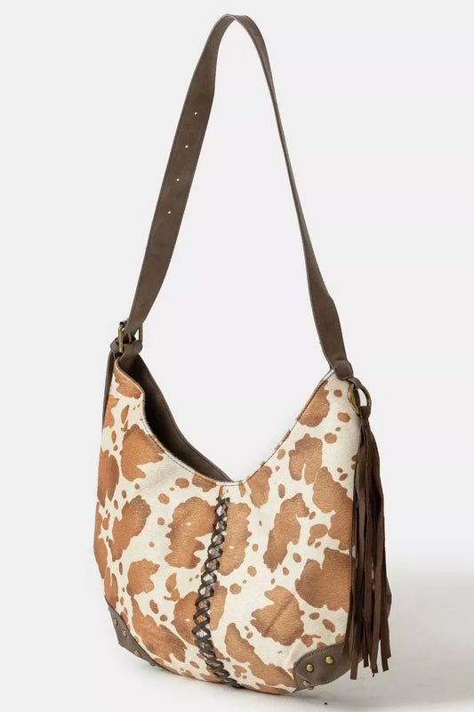 cow print handbag with brown leather strap on a white background