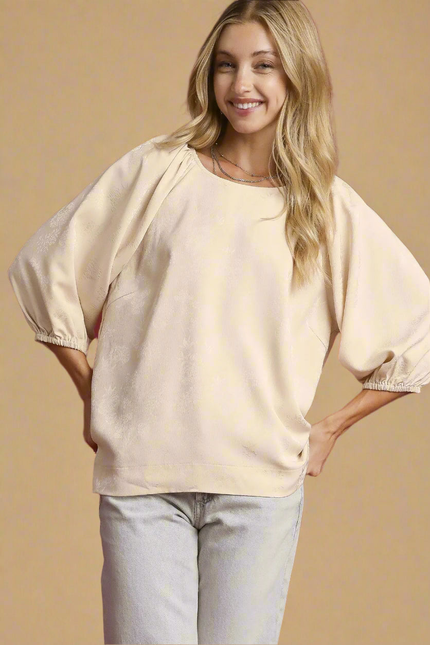 Woman wearing a beige blouse with balloon sleeves against a beige background