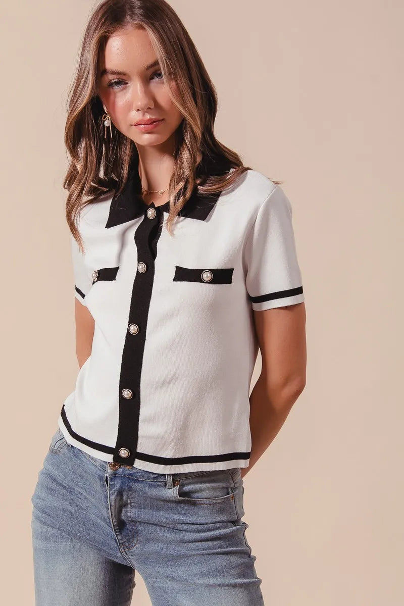 Woman wearing a white blouse with black accents and blue jeans on a beige background