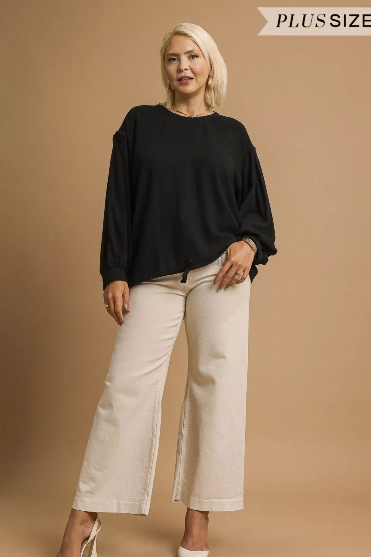 Woman wearing a black top and beige pants on a brown background