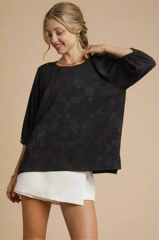 Woman wearing a black floral blouse and white shorts on a beige background