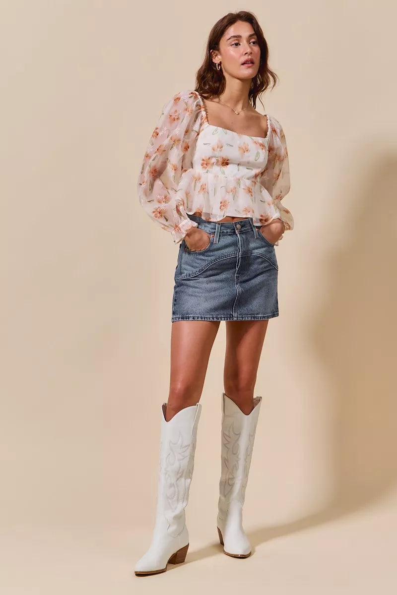 Woman wearing a floral top, denim skirt, and white cowboy boots on a beige background