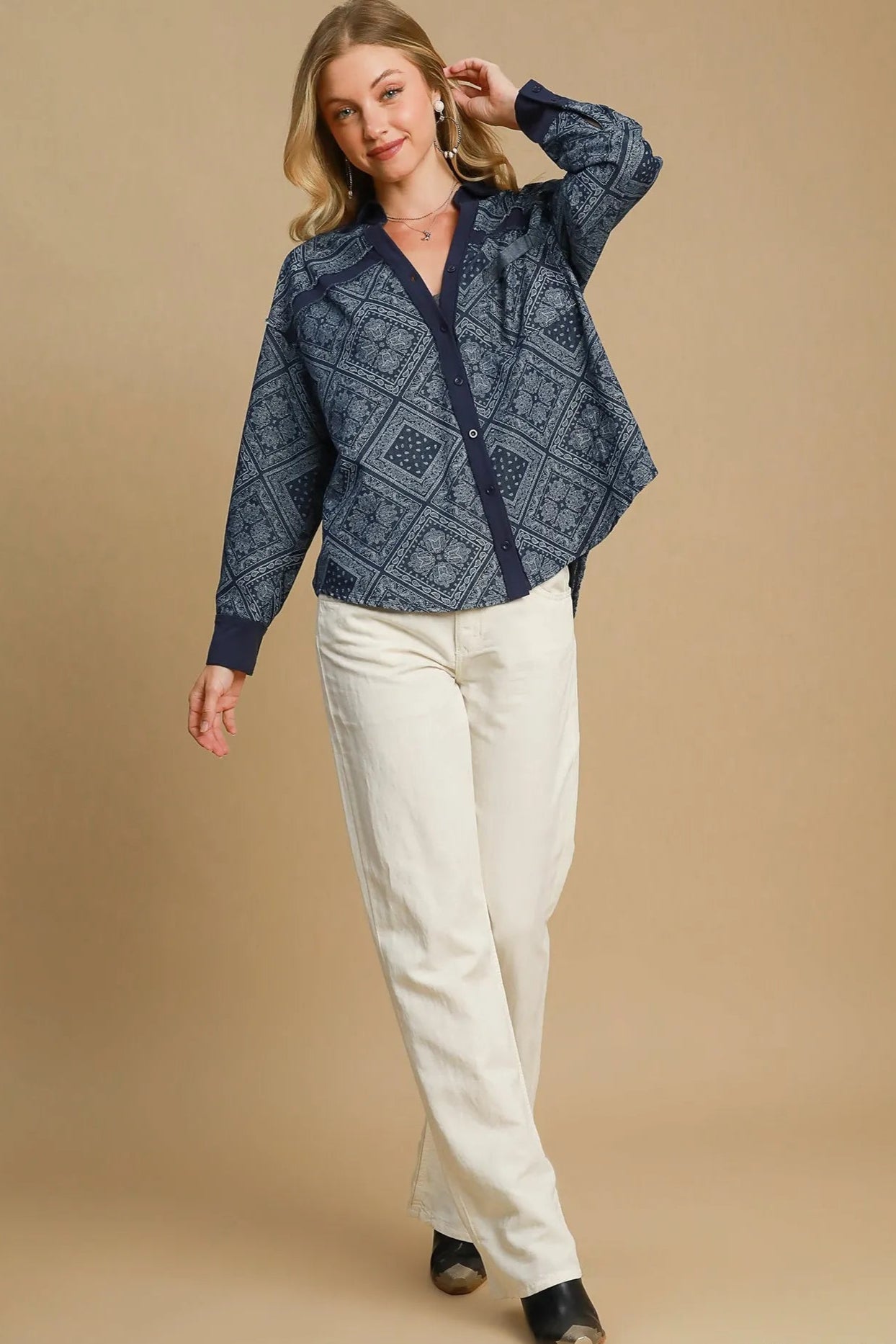 Woman wearing a blue patterned shirt and white pants on a beige background