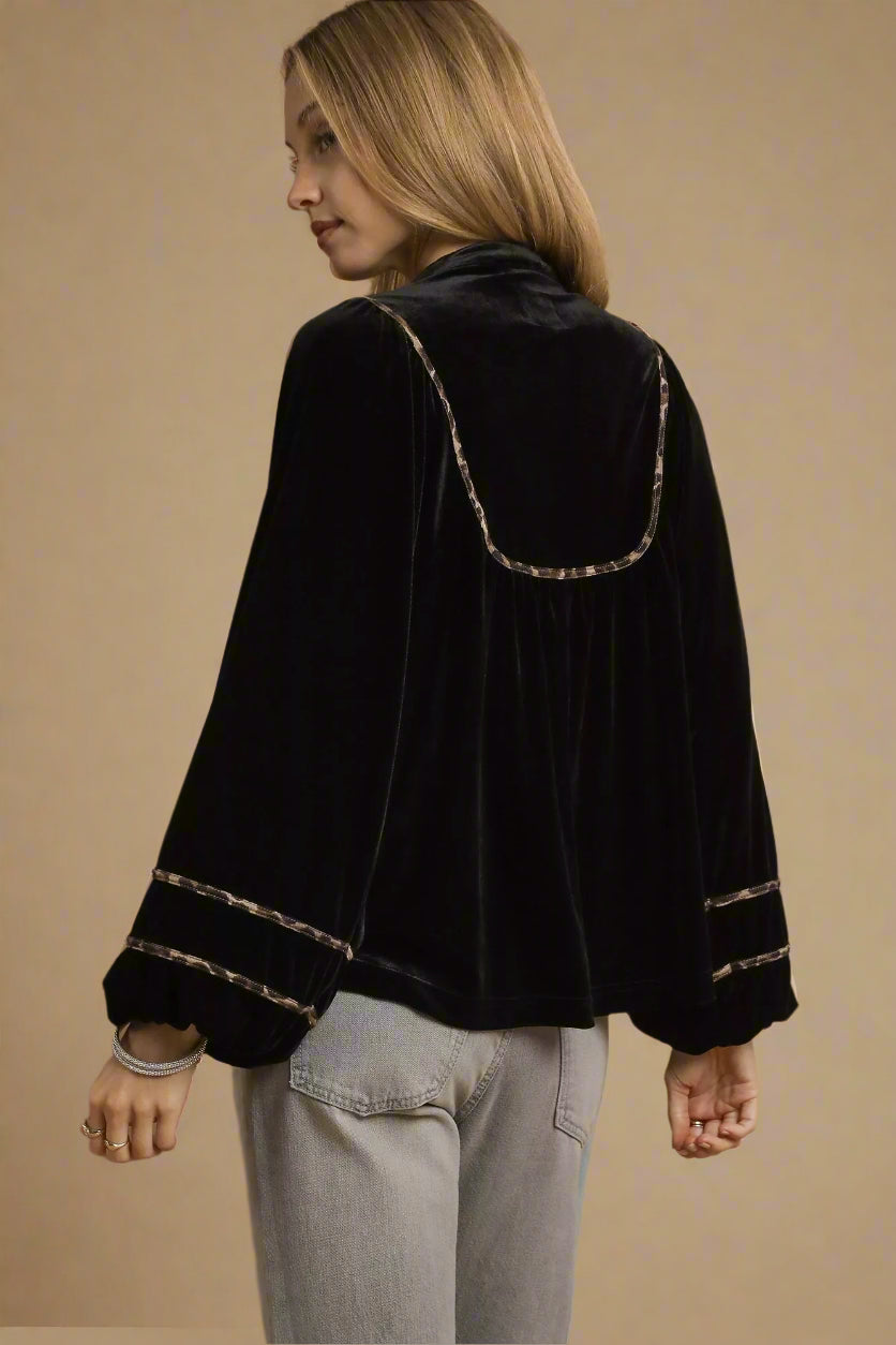 Woman wearing a black velvet jacket with decorative trim on a beige background