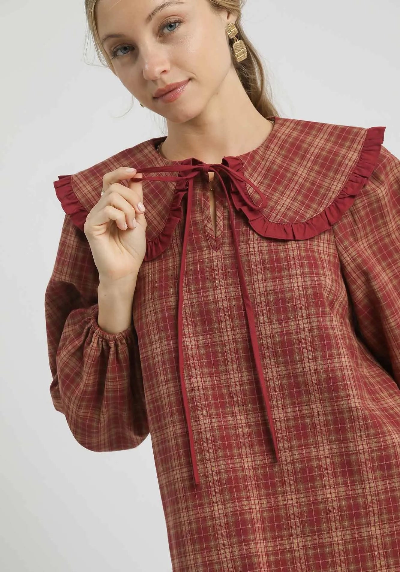 Woman wearing a red plaid dress with a ruffled collar on a white background