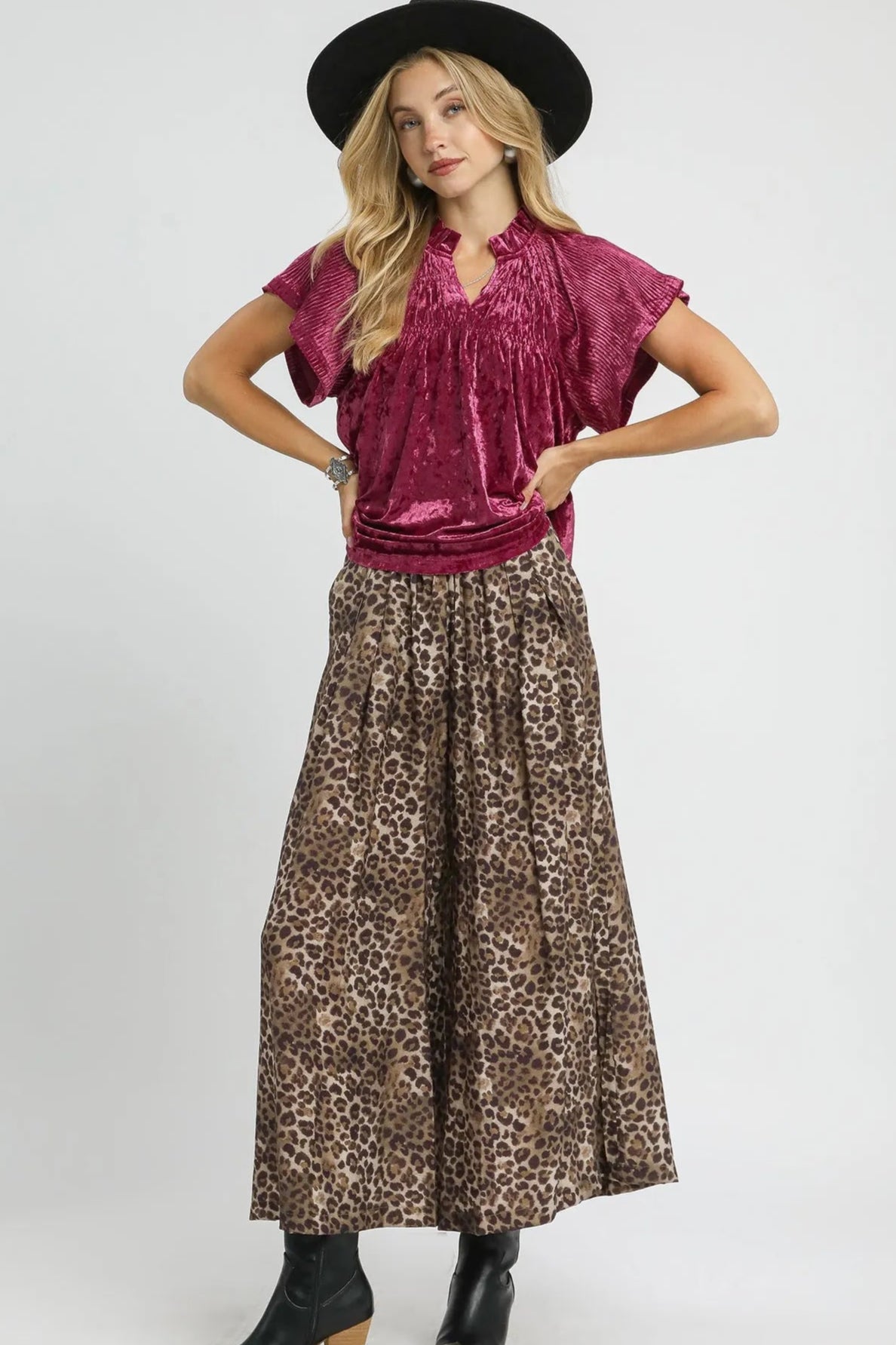 Woman wearing a burgundy top and leopard print skirt with a black hat on a white background