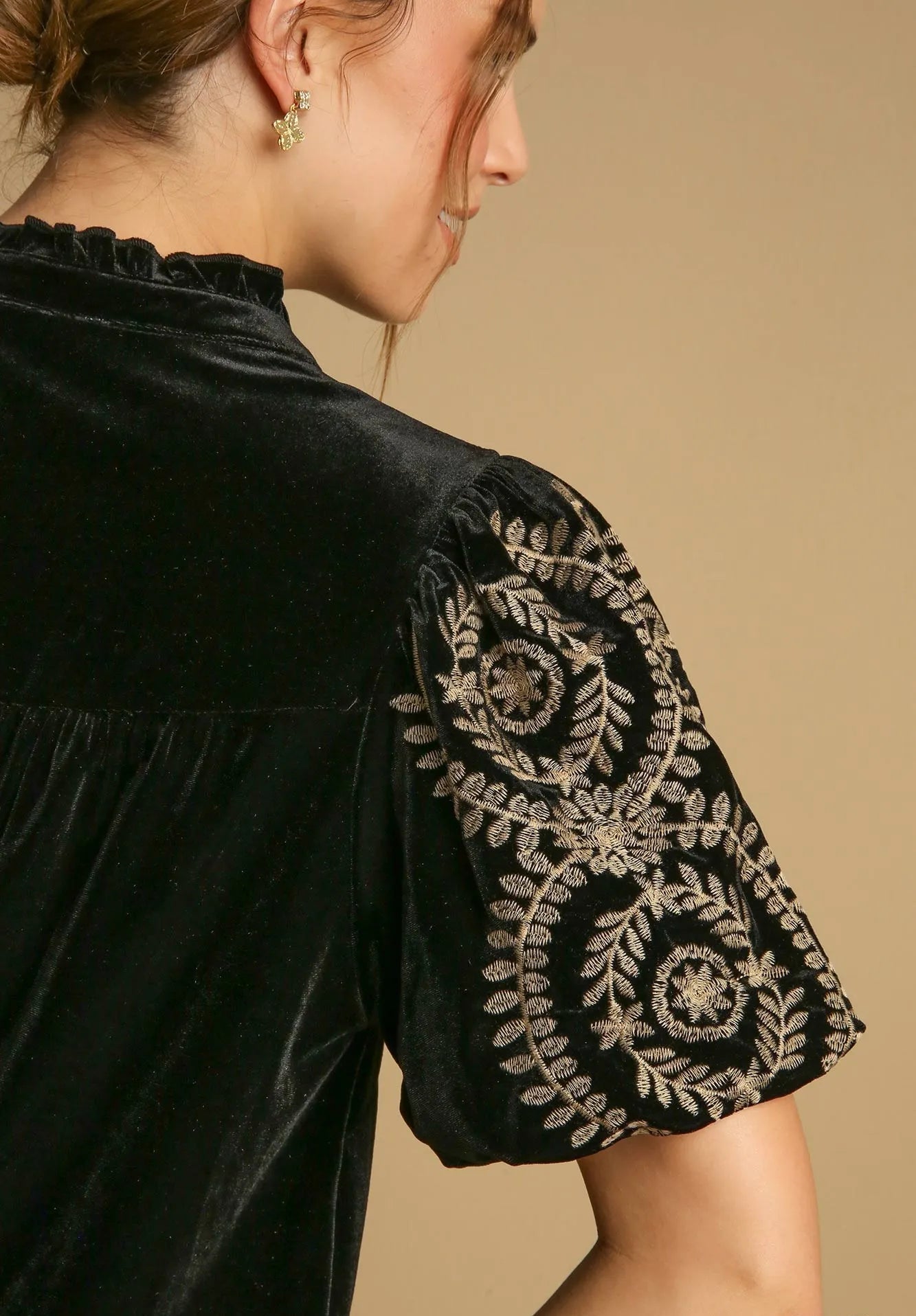 Black blouse with intricate gold embroidery on sleeves against a beige background