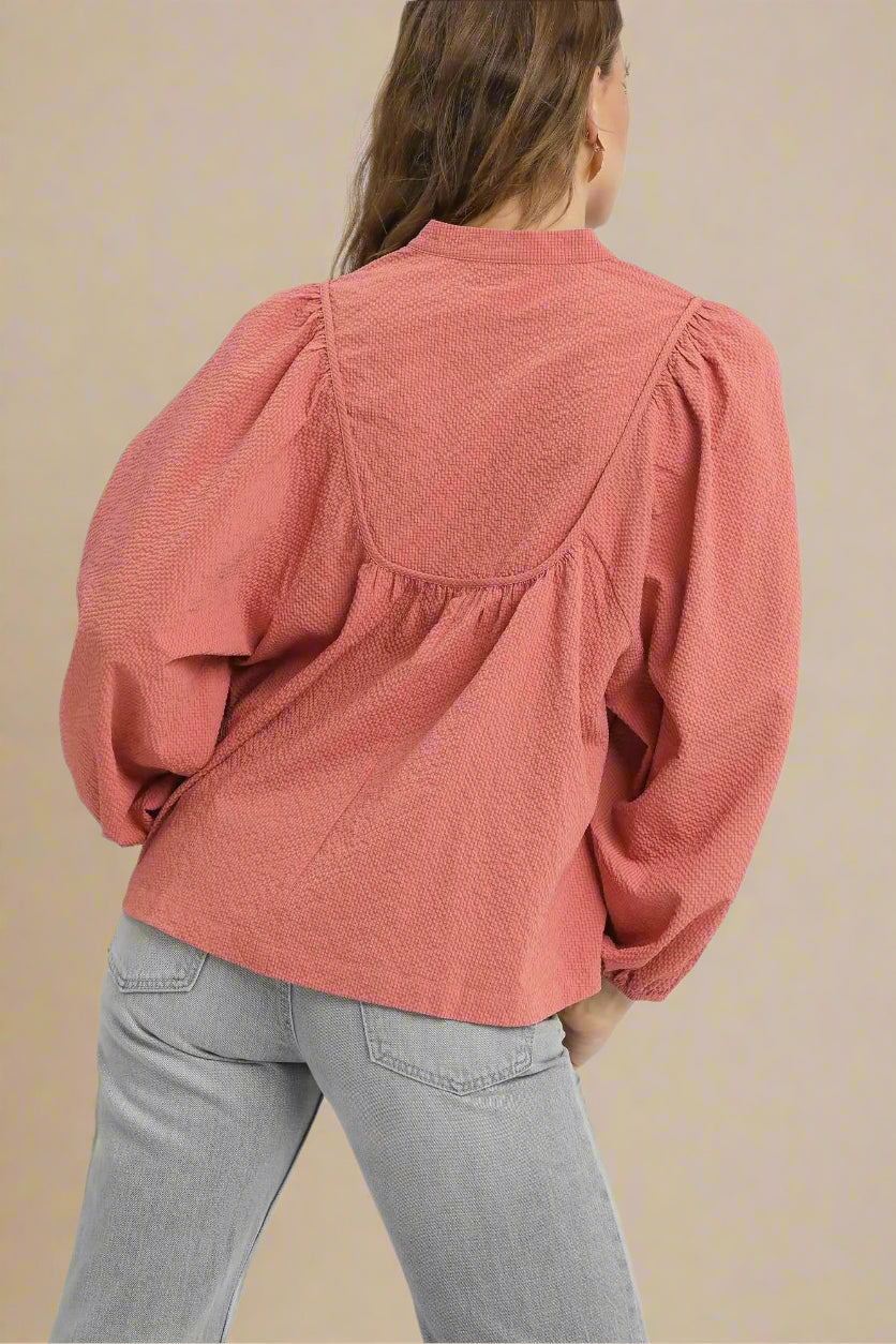 Person wearing a dusty rose blouse with puffed sleeves on a beige background