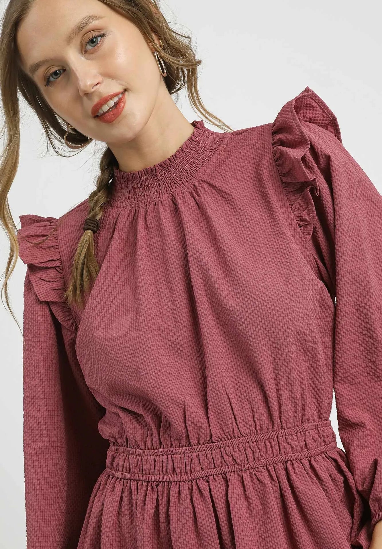 Woman wearing a dusty rose dress with ruffled shoulders against a white background