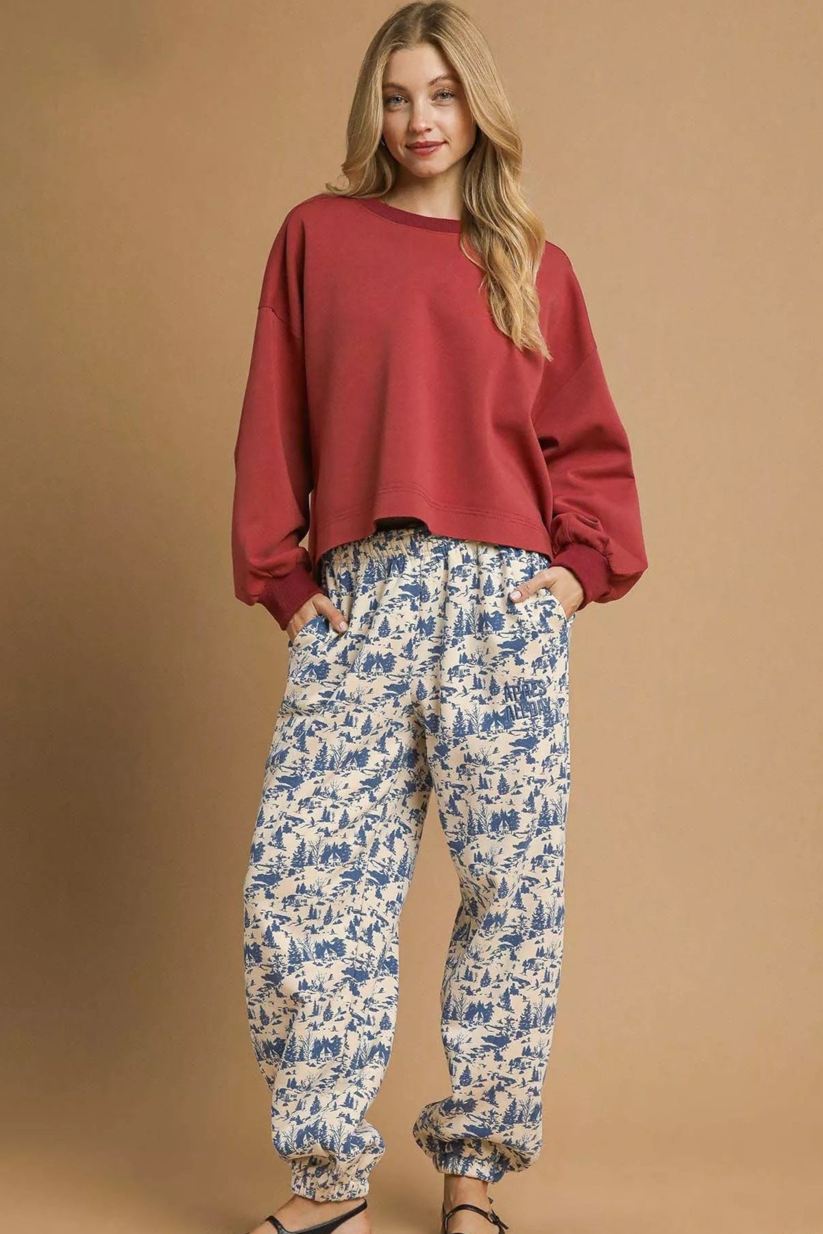 Woman wearing a red sweater and patterned pants on a beige background